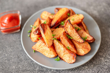 Baked potato wedges with herbs and sauce on stone background - homemade organic vegetable veggie...