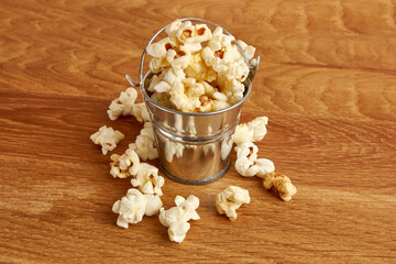 Small bucket filled with popcorn on a wooden background.
