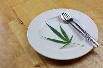 Marijuana leaves in a plate with spoon and fork on a wooden table