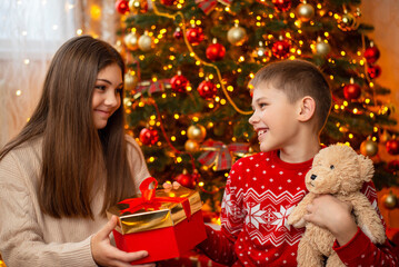 Little boy with teddy bear giving Christmas present to his sister. Christmas celebration concept
