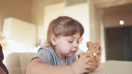 children eat burgers. fast food burger. a group of small children in the kitchen greedily eat fun fast food burgers. big family small kids having breakfast in the morning in the kitchen eating burger