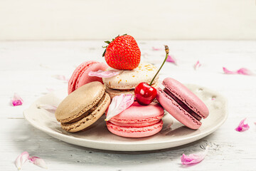 Macarons with strawberries, cherries and peonies flower petals, on a white wooden background