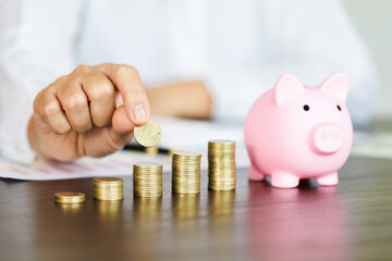 stacks of coins in a row and pig piggy bank on the table and woman picking up a coin for save money, saving money or savings concept.