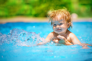Fototapeta na wymiar The baby is learning to swim. The child has fun outdoors in the pool in the villa. Family happiness. Little beautiful girl is splashing in the pool