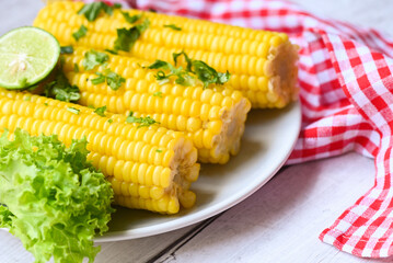 sweet corn food with salad vegetable lime coriander and lettuce, sweet corn cooked on white plate background, ripe corn cobs steamed or boiled sweetcorn for food vegan dinner or snack