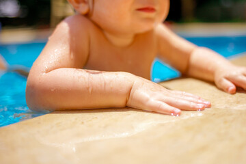 The baby is learning to swim. Family happiness. Little beautiful girl is splashing in the pool. The...
