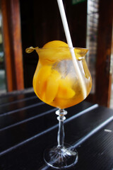summer orange non alcoholic cocktail with pieces of peach and paper straw