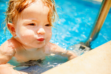 Little beautiful girl is splashing in the pool. The baby is learning to swim. The child has fun...