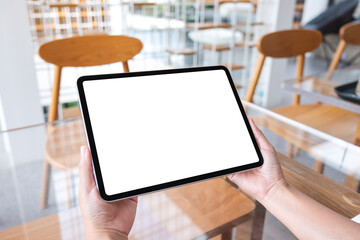 Mockup image of a woman holding digital tablet with blank white desktop screen in cafe
