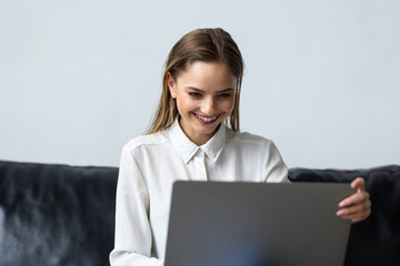 Relaxed woman using laptop in luxury home living room with big window, enjoying working, internet shopping, checking social network with computer sitting on sofa