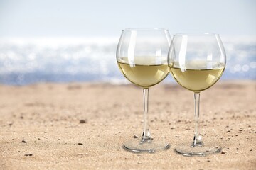 Two glasses of cold rose wine on sandy beach in sunny day,