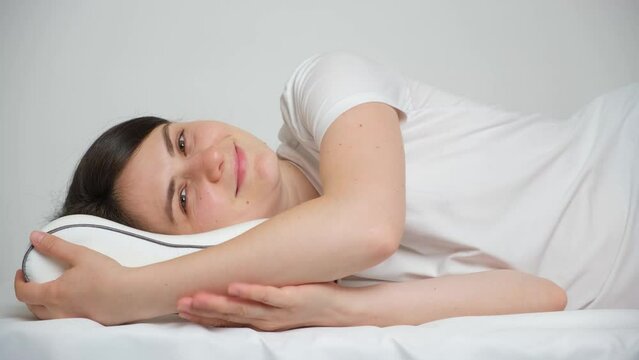A woman lies on an orthopedic pillow made of memory foam and smiles looking into the camera.