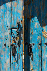 A part of old worn looking blue painted door with black wrought iron latch and handle 