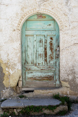 Fototapeta na wymiar Old wooden arched light cyan door in an old cracked white wall. 
