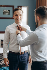 Two friends before an important wedding day. One helps the other to put on a tie and straightens the suit. The groom morning.