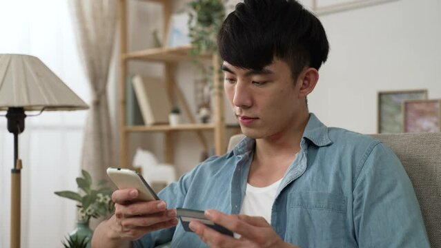 closeup view of an asian man using credit card to pay on the mobile phone while shopping online in the living room at home during covid19 lockdown.