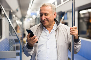 Elderly passenger is engrossed in information on smartphone while traveling in subway car