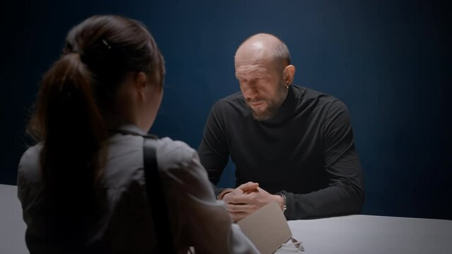 Female detective interrogates suspected criminal in handcuffs. Police officer opens dossier folder with evidence. FBI agent asks to sign papers. Arrested mafia refuses to talk to cop without lawyer