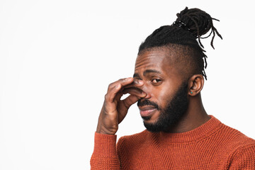 Young african-american man in red sweater with dreadlocks smelling stinky, closing nose with a hand because of odor stench isolated in white background - obrazy, fototapety, plakaty