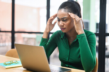 Worried african-american female employee colleague staring at laptop screen sitting on the...