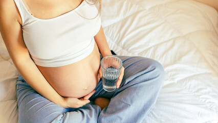 Pregnant water drinking woman. Young pregnancy mother drink water. Pregnant lady waiting of baby. Glass of water. Concept of maternity, expectation.