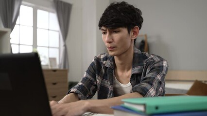 asian male student having trouble finding answer on computer for his schoolwork is looking at screen with frustrated face while learning from home in his bedroom