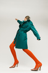 Side view portrait of stylish girl in green coat and bright orange tights dancing isolated over...