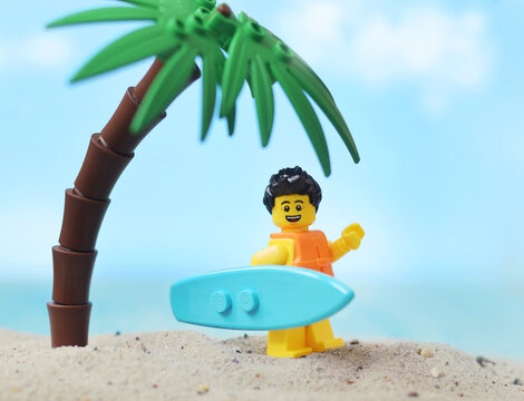 Lego minifigure surfer with surfboard on sandy beach. Editorial illustrative image of popular children constructor toy.