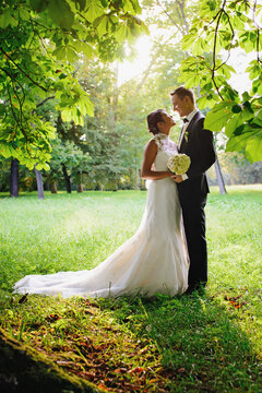  Beautiful bride in a long white dress. Handsome groom in a black suit. Couple in a summer park