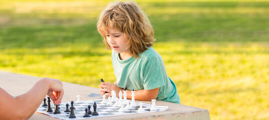 Father and son play chess outdoor, banner poster with copy space, son kid playing chess on table in...