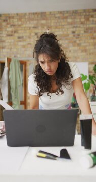 Vertical video of biracial female artist working on laptop in studio