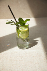Drink in a glass with mint, rosemary, lemon and lime on a stone table with shadow. Summer drink lemonade with an iron tube