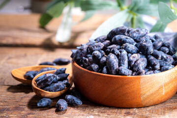 Bowl with fresh  raw farm haskap berry, garden grown honeysuckle, honeyberry, on wooden background copy space