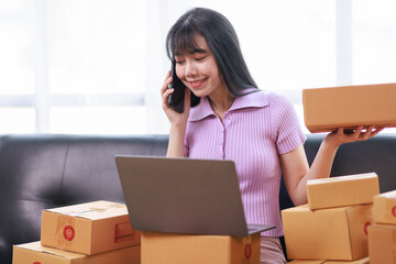 Startup SME small business entrepreneur of freelance using a laptop with box, Asian business woman on sofa check online orders to prepare to pack the boxes sell to customers sme business ideas online.