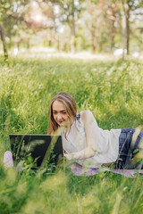 Naklejka na ściany i meble the girl sits on the grass and uses a laptop. Education, lifestyle, technology concept, outdoor learning concept