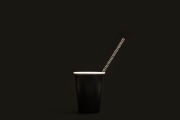 Vaso de cartón negro con pajita con rayas blancas y negras sobre un fondo negro liso y aislado. Vista de frente y de cerca. Copy space
