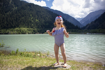 a beautiful little girl in a swimsuit and a bathing cap by a mountain lake. a fun time. summer. mountain landscape.