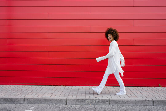 Smiling woman walking on sidewalk by red wall