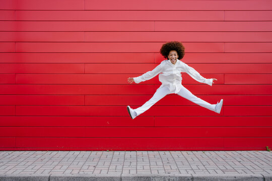 Cheerful young woman doing splits in front of red wall