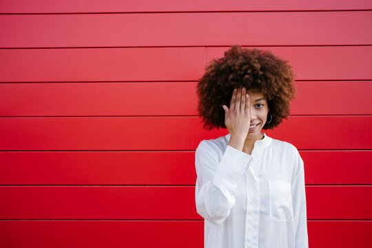 Smiling woman covering half face with hand in front of red wall