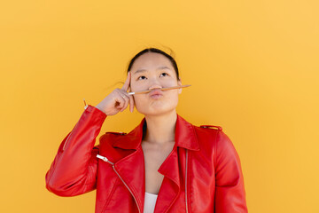 Playful woman with pencil on puckering lips against yellow background