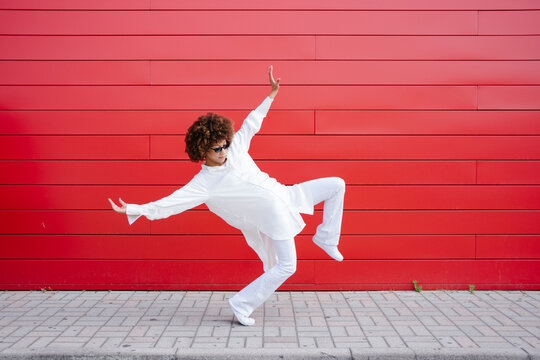 Young Afro woman balancing on footpath by red wall