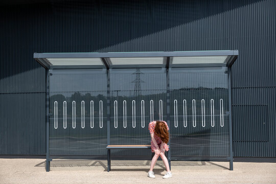 Sad young woman sitting alone at bus stop
