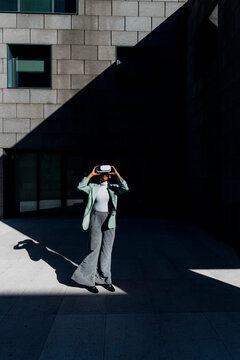 Young businesswoman wearing VR goggles in front of office building