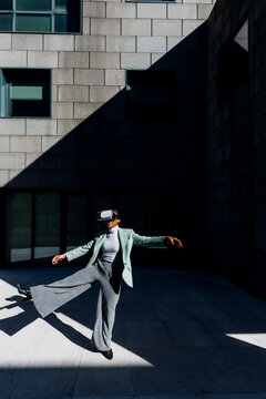 Businesswoman with virtual reality standing on one leg in front of office building