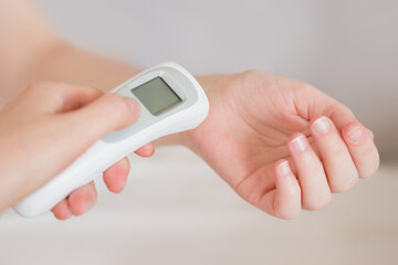 A woman's hand applies an infrared thermometer to measure body temperature © Evgenia