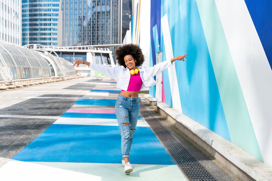 Smiling young woman with arms outstretched walking by colorful wall