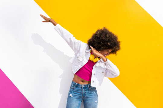 Playful young Afro woman doing dab dance in front of colorful wall