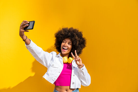 Happy woman taking selfie through mobile phone in front of yellow wall