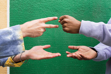 Hands of friends playing rock paper scissors in front of green wall
